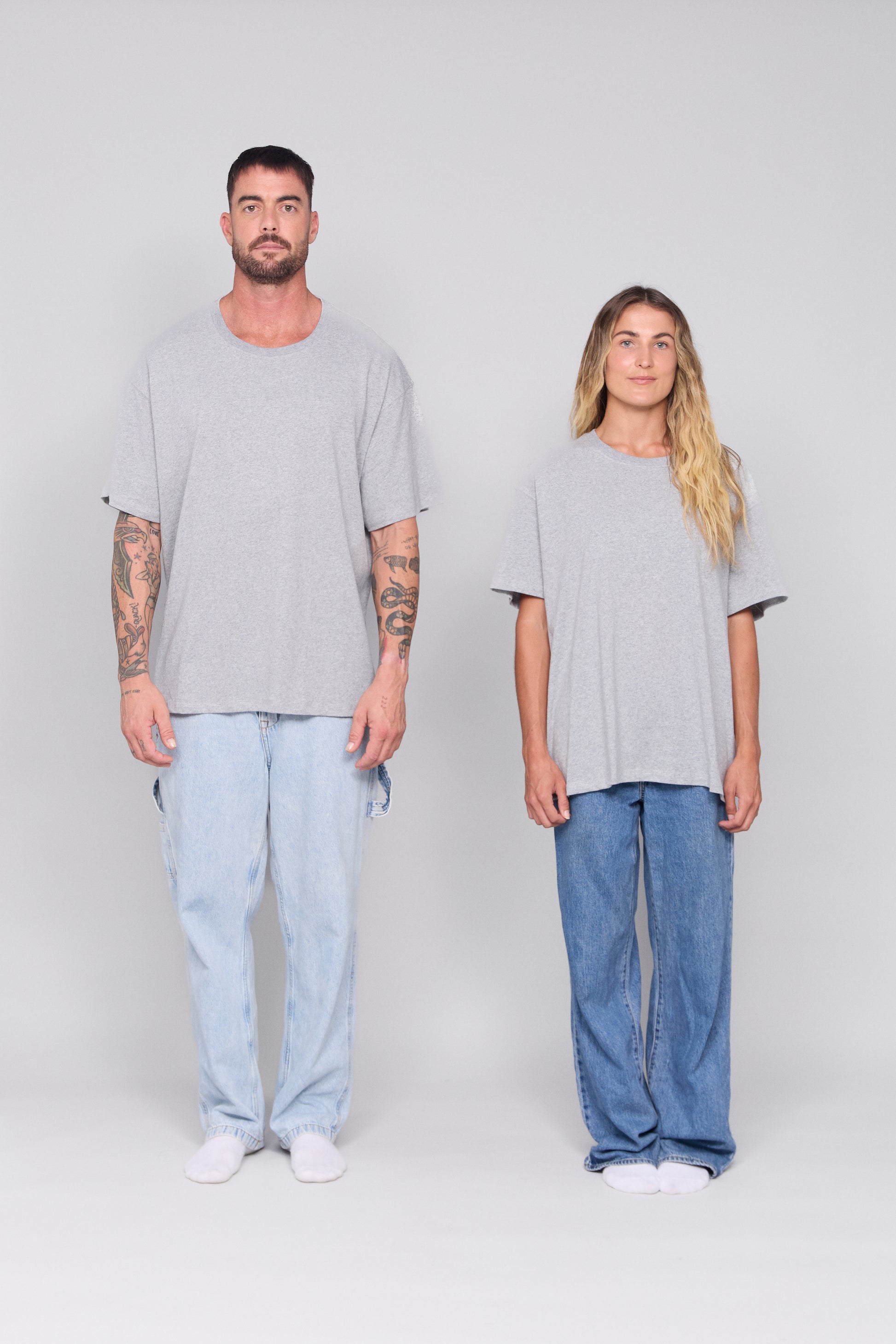 Two people wearing matching gray oversized t-shirts and blue jeans on a plain background