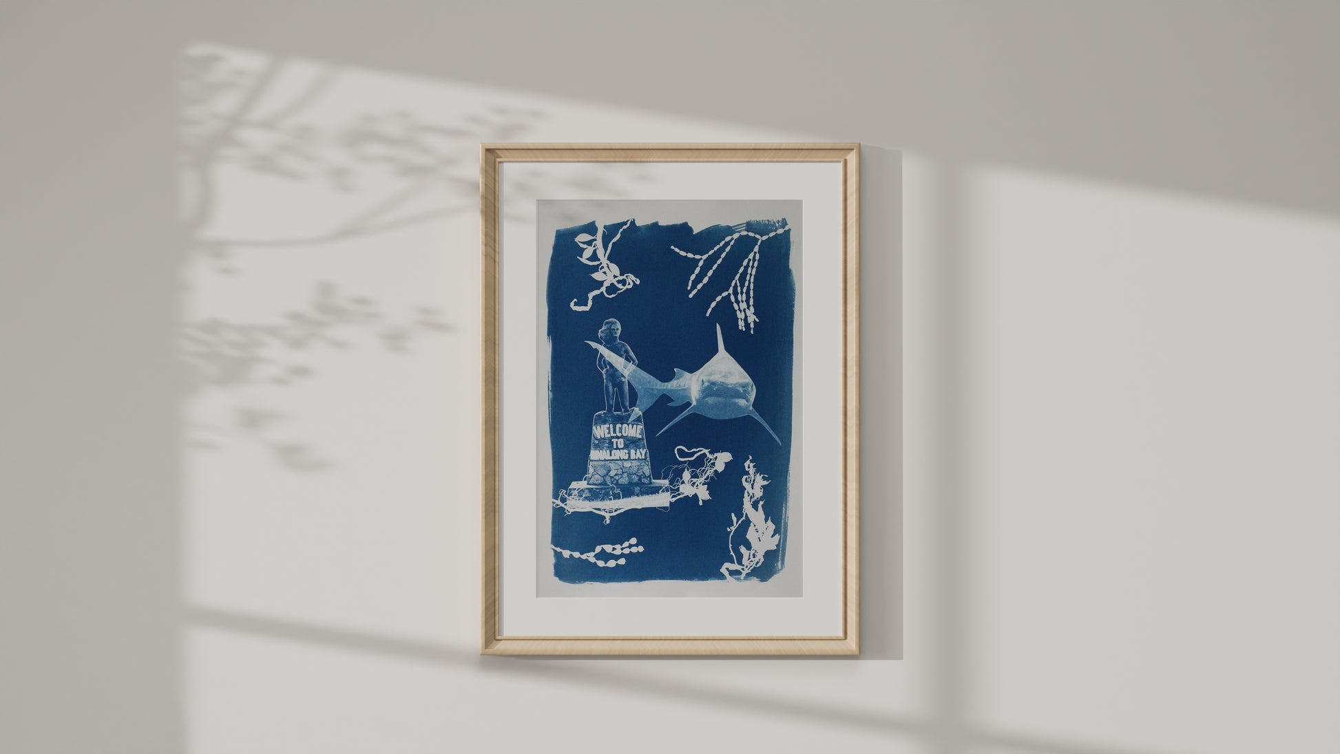 A framed art print featuring a blue and white ink-style illustration of a shark and marine elements, displayed on a light gray wall with soft shadow overlays.