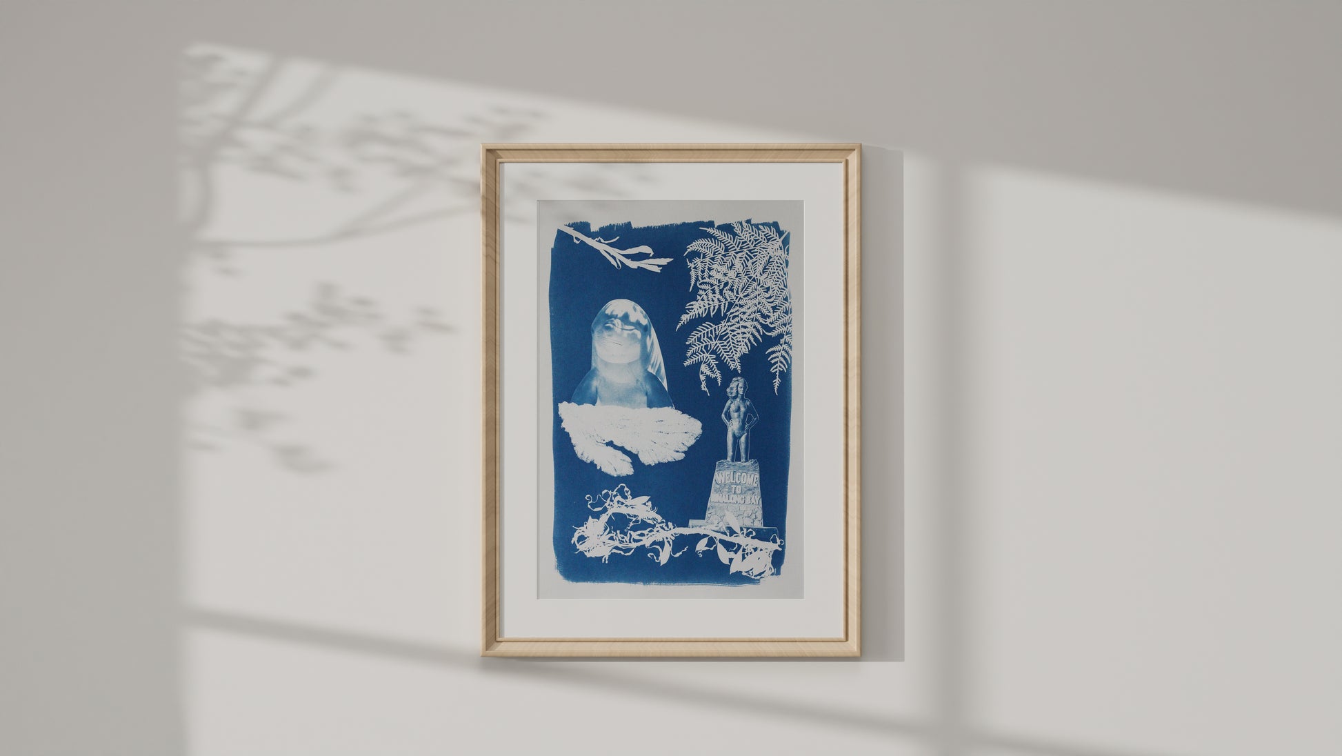 Framed art print of a cyanotype print featuring a dolphin, various seaweed pieces, a fern and the Syrena of Binalong Bay statue. 