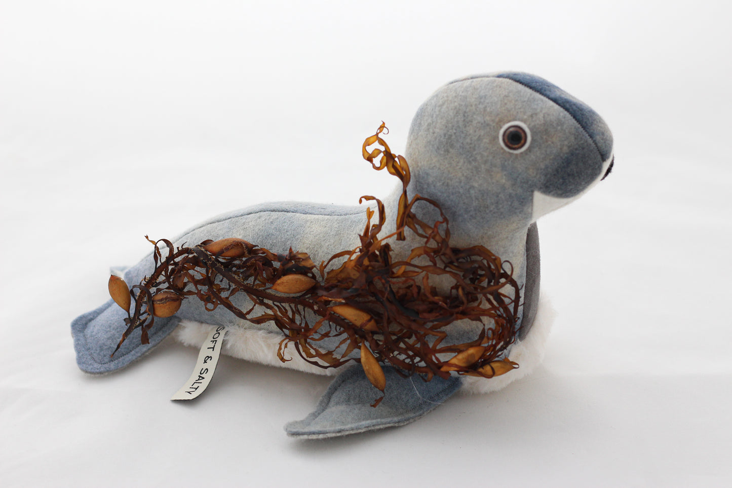 Stuffed seal toy with seaweed on a white background