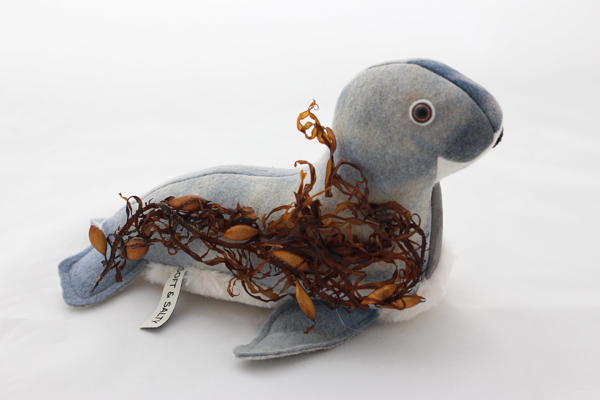 Stuffed seal toy with seaweed on a white background