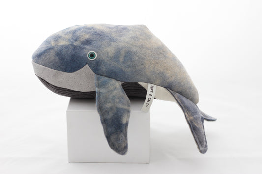 Plush whale toy on a white cube with a white background