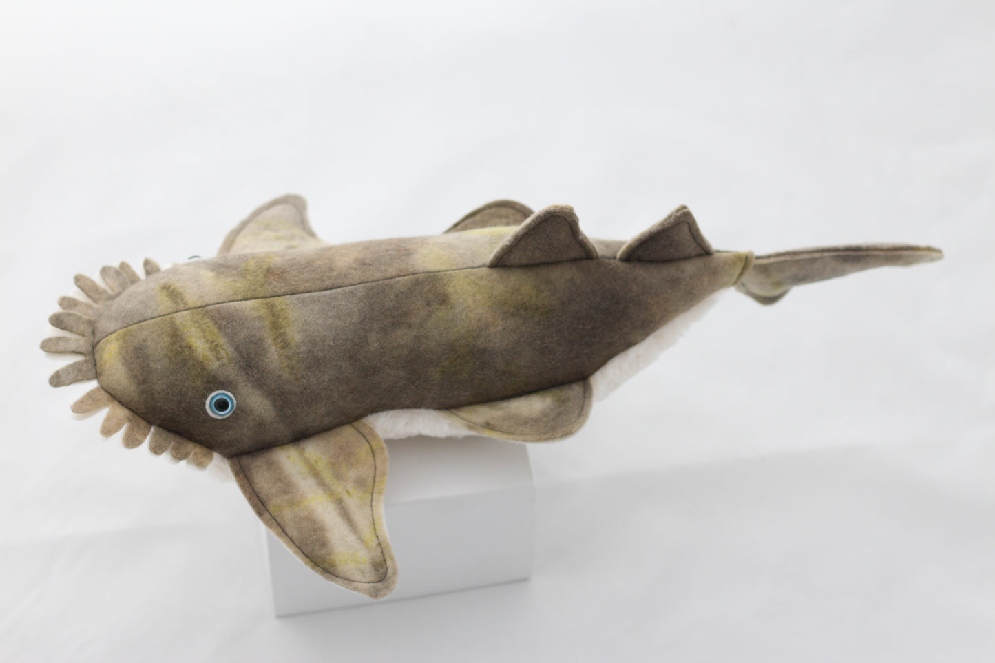 Plush toy wobbegong shark on a white stand with a white background