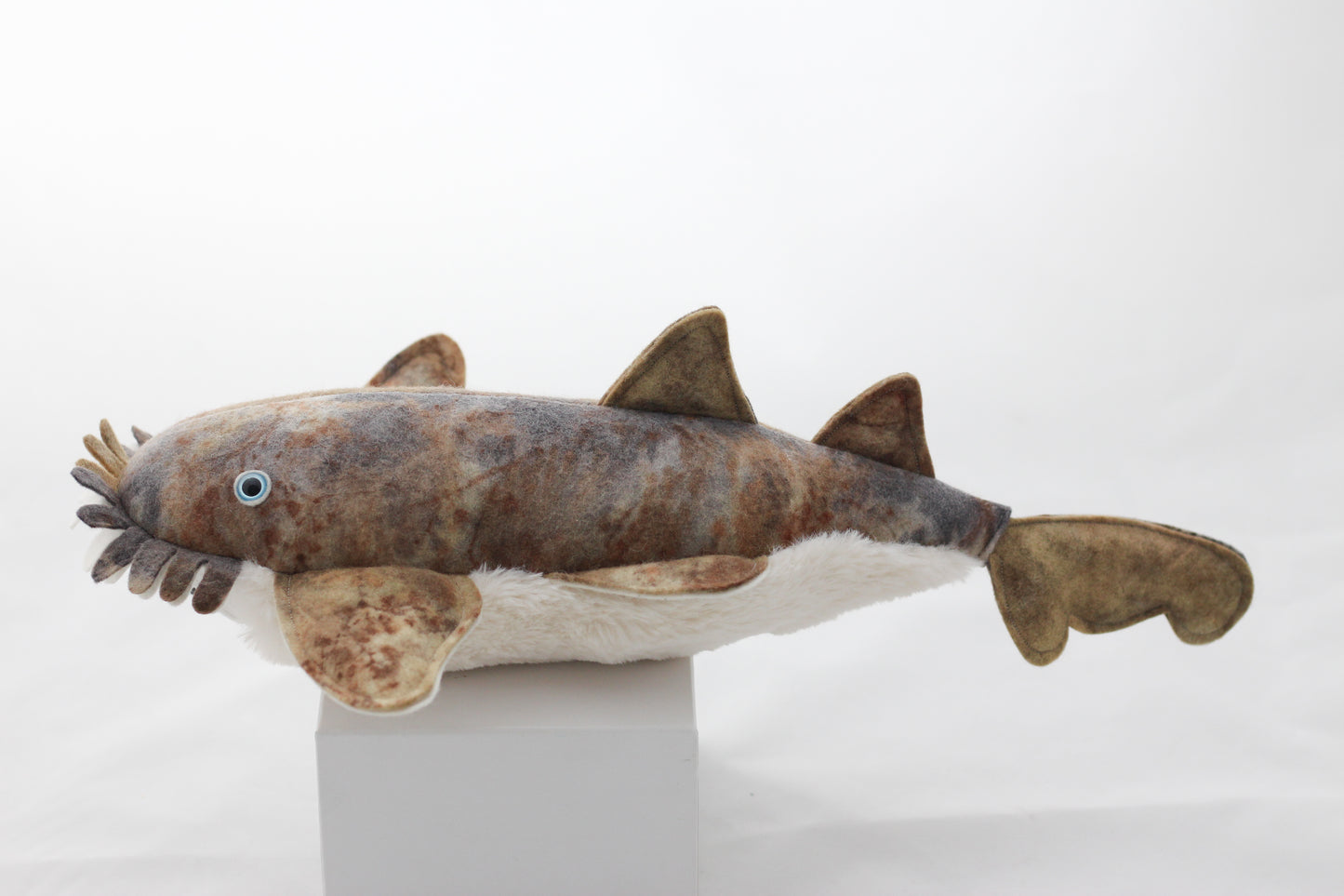 Plush wobbegong shark toy on a white pedestal with a white background