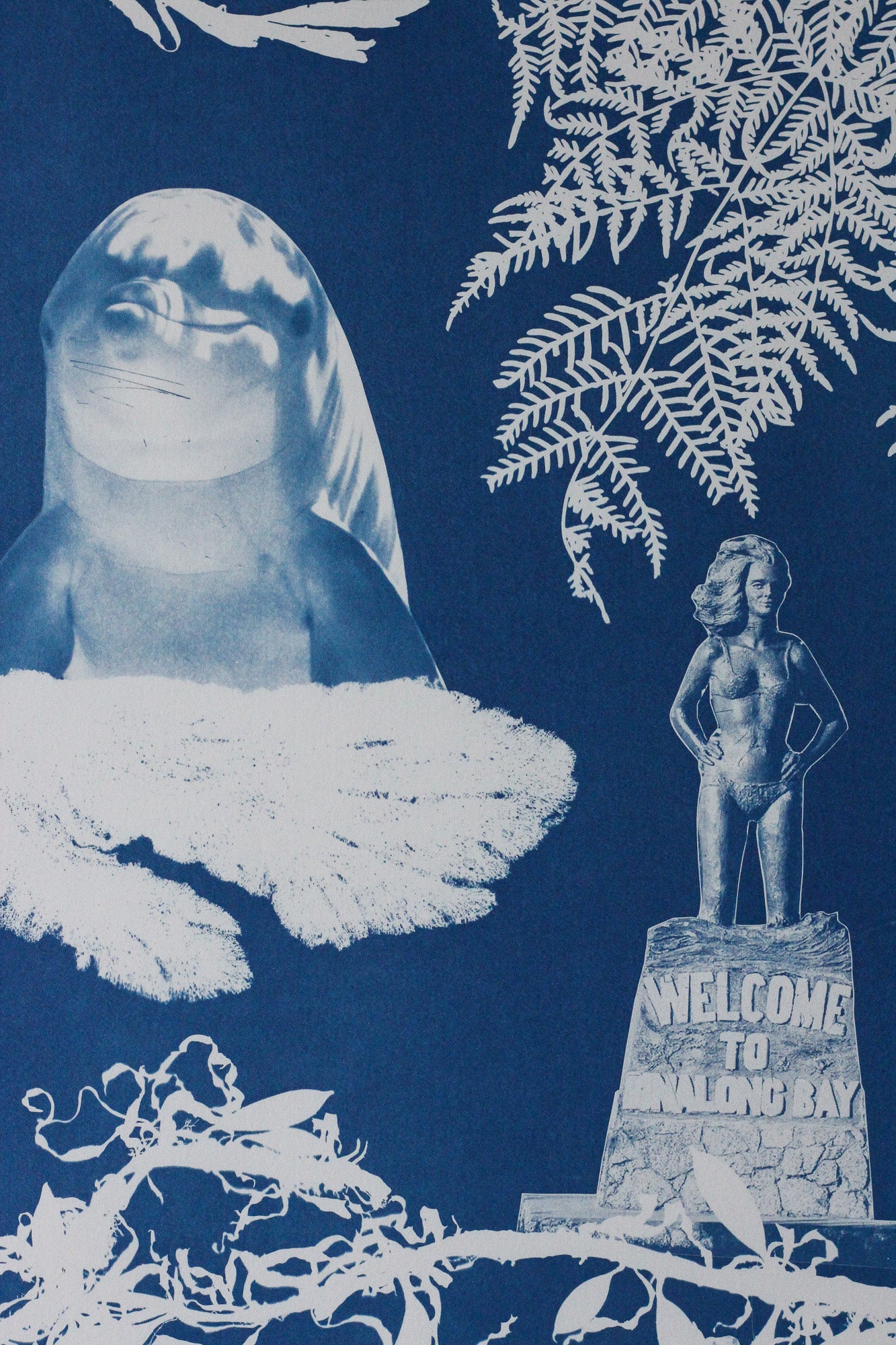 Close up of a cyanotype on paper artwork featuring a dolphin, various seaweed pieces, a fern and the Syrena of Binalong Bay statue. 