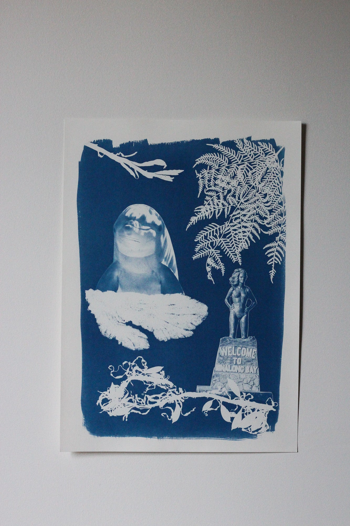 Cyanotype on paper artwork featuring a dolphin, various seaweed pieces, a fern and the Syrena of Binalong Bay statue. 