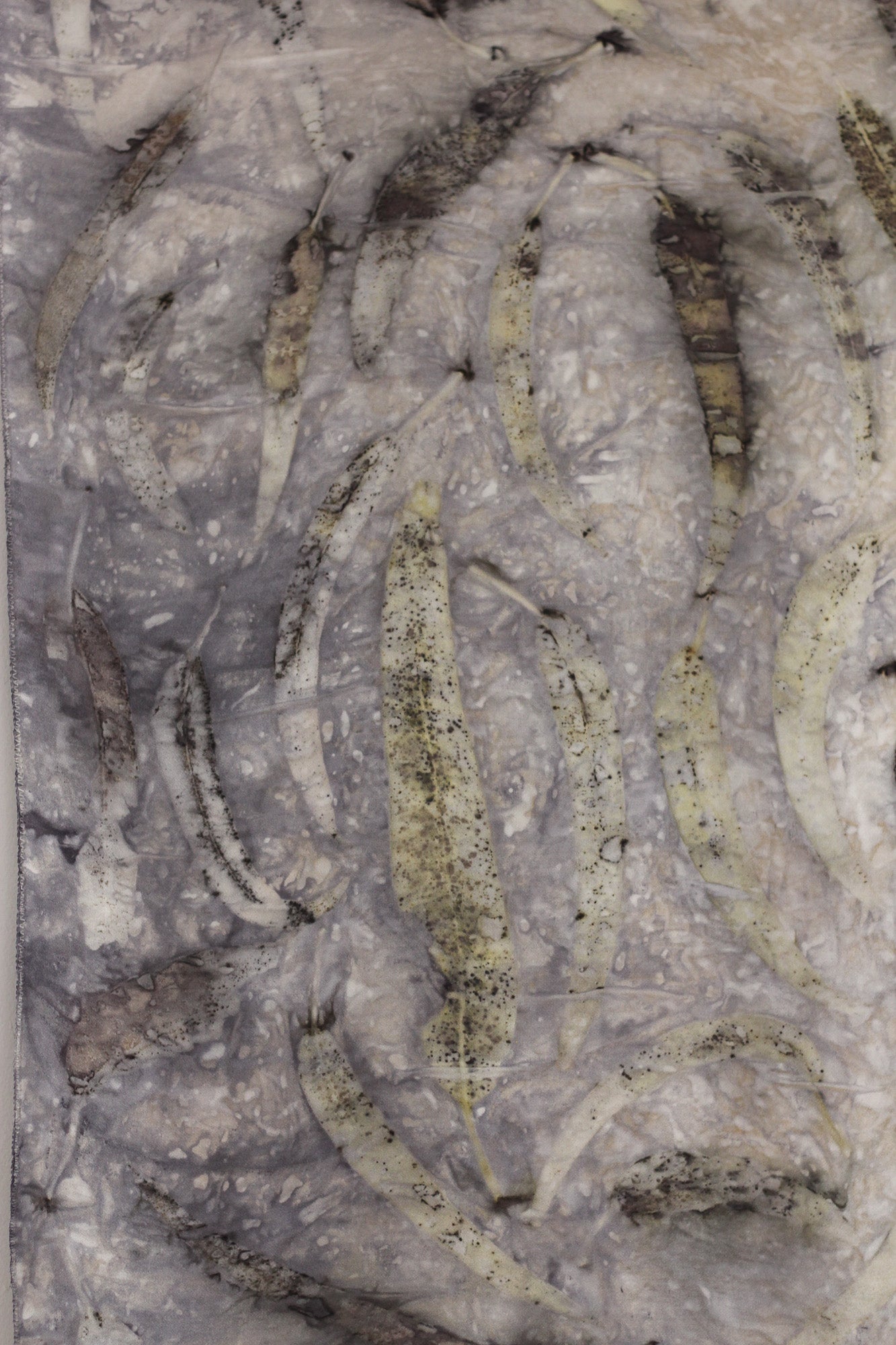 A close up of a botanical print on silk fabric featuring eucalyptus leaves and natural smokey tones. 