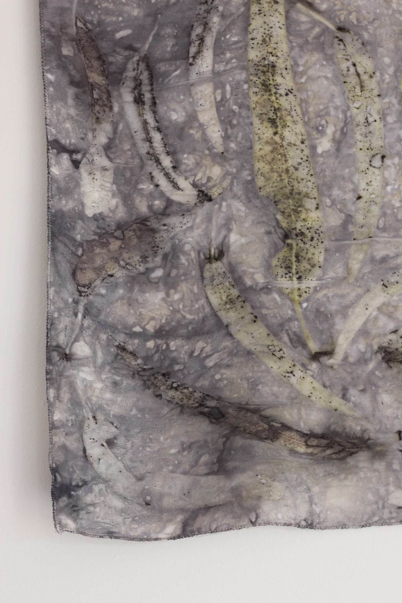 A close-up of a textured gray and white fabric surface with elongated leaf-like patterns and speckled details, photographed against a plain white background.