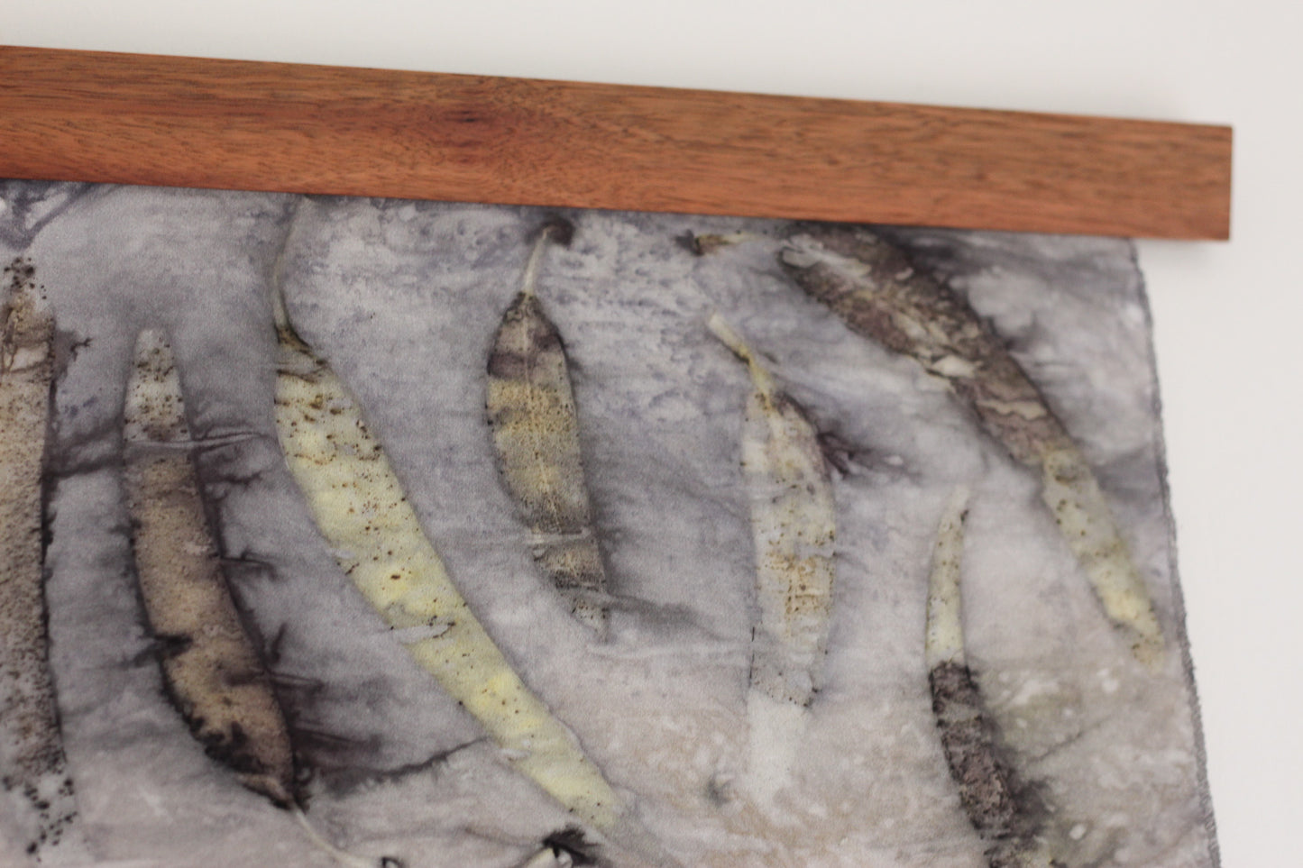 A close-up of a textured gray fabric panel featuring several eucalyptus leaf prints, with a wooden strip along the top edge.