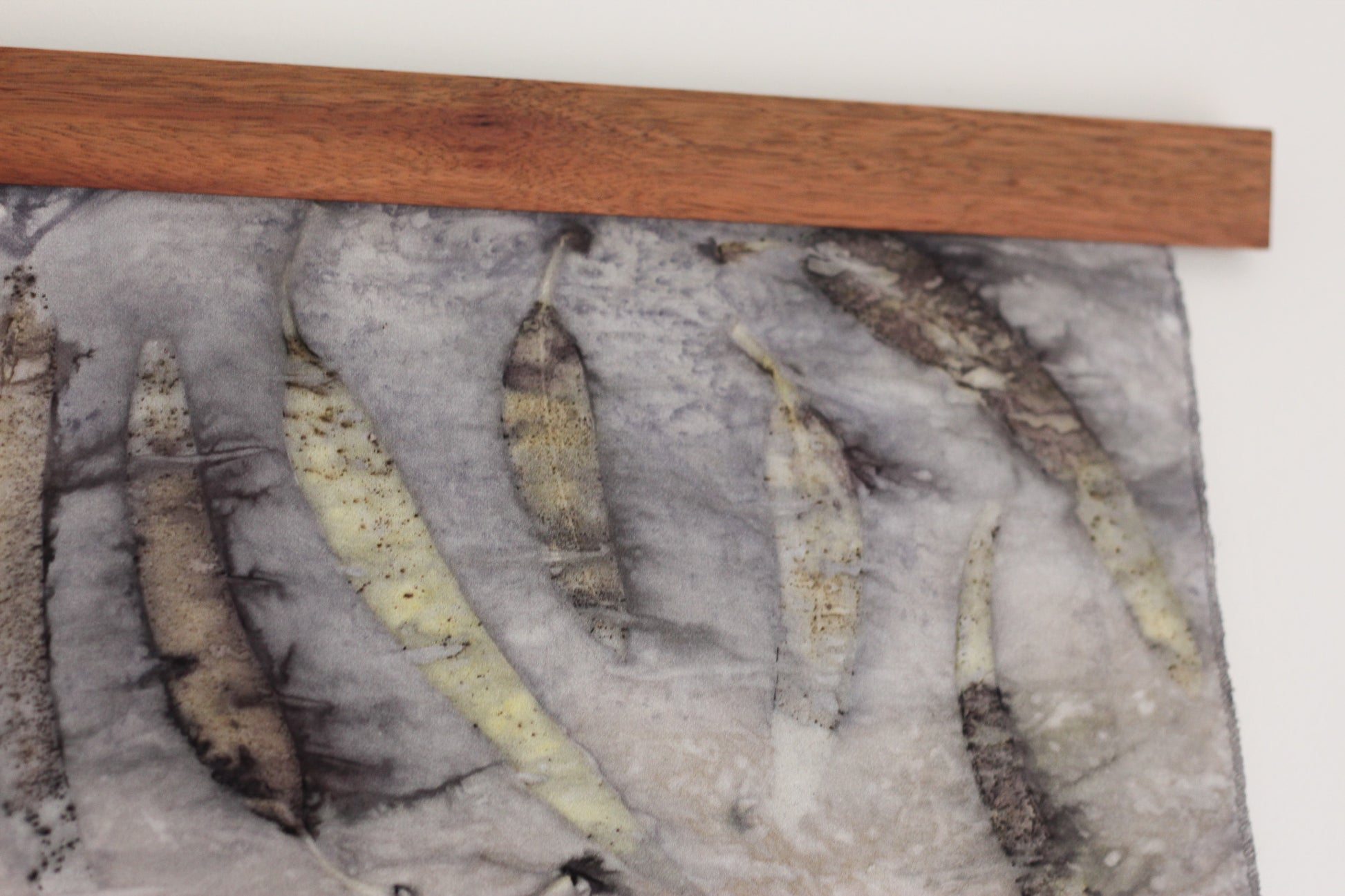 A close-up of a textured gray fabric panel featuring several eucalyptus leaf prints, with a wooden strip along the top edge.