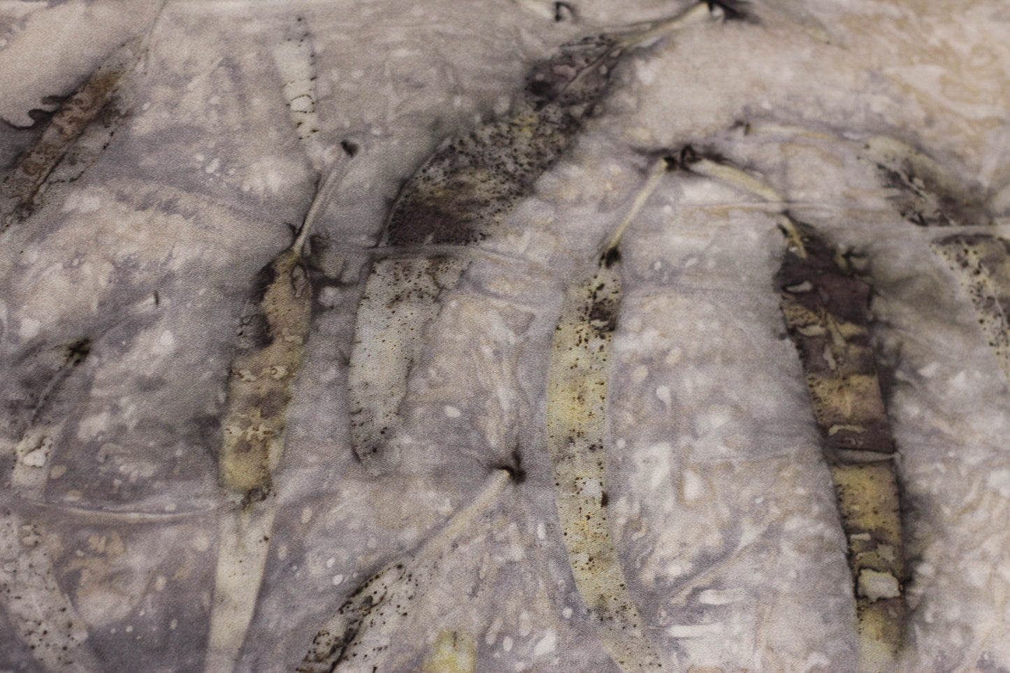 A close-up of a textured surface featuring a repeating pattern of dried leaves in muted brown, gray, and beige tones.