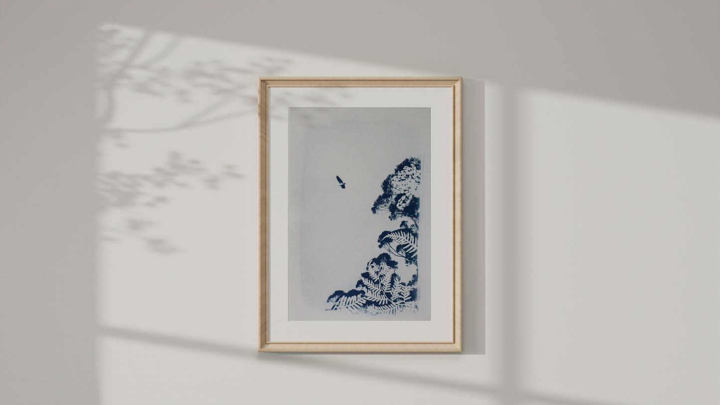 A framed art print featuring a cyanotype print of a sea eagle and tree on a white background, housed in a light wood frame and mounted on a white wall with soft shadow projections.